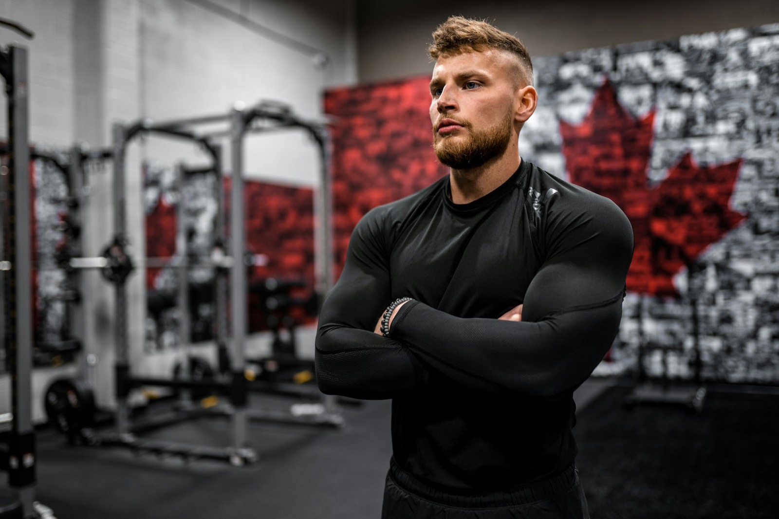 Athlete in a black long-sleeve compression top, arms crossed, in a strength gym